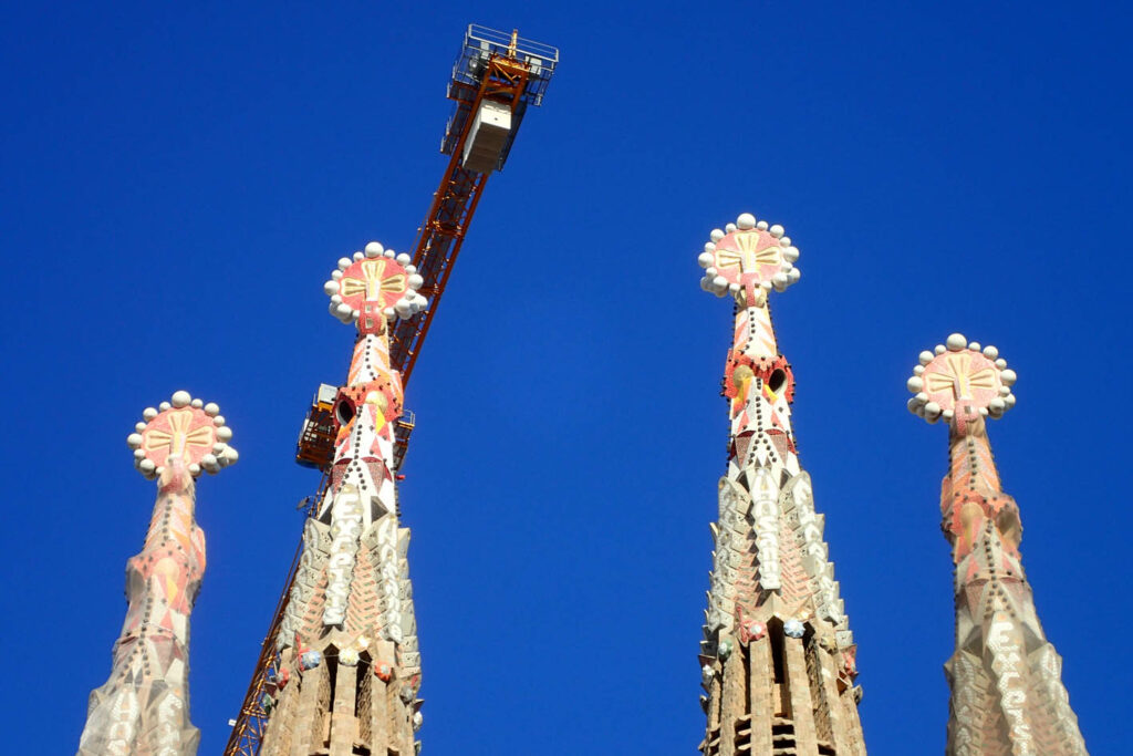 Ornate spires on top of La Sagrada Familia in Barcelona with blue sky and a crane in the background
